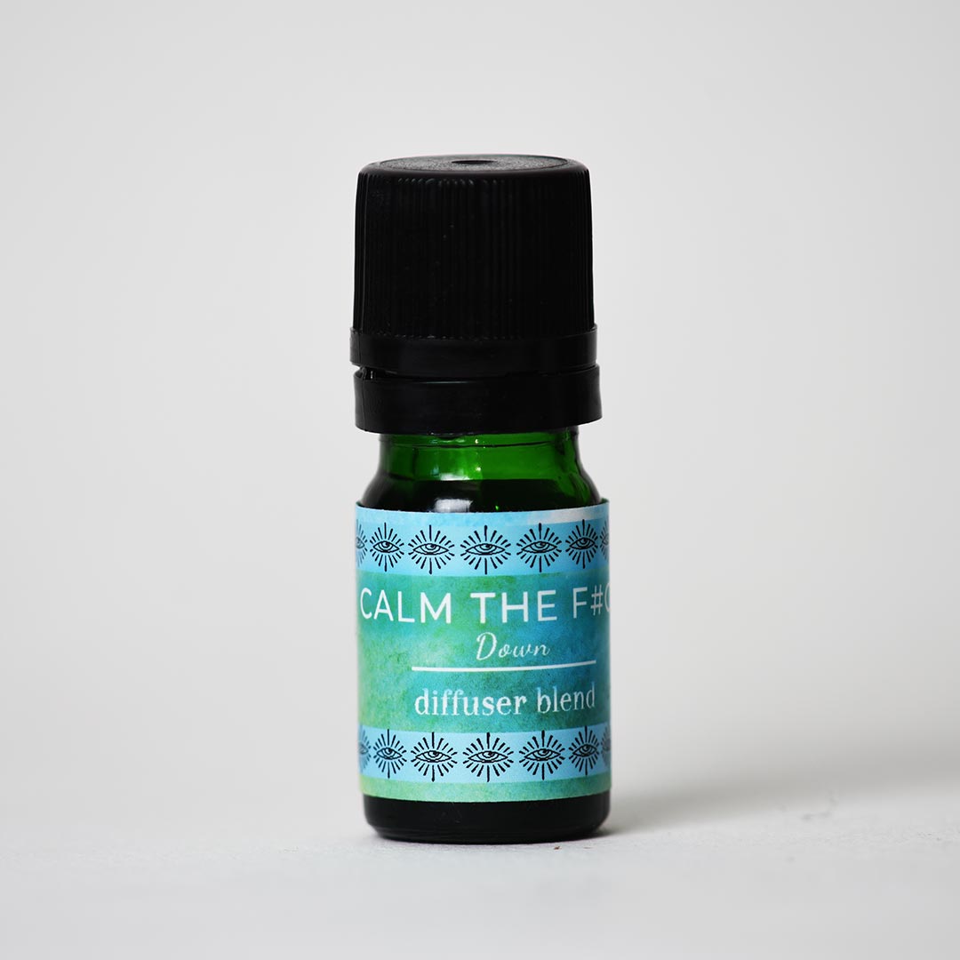 A small dark green glass bottle with a black ribbed cap and a blue-green label reading 'CALM THE F# DOWN essential oil diffuser blend', photographed on a plain light gray background.