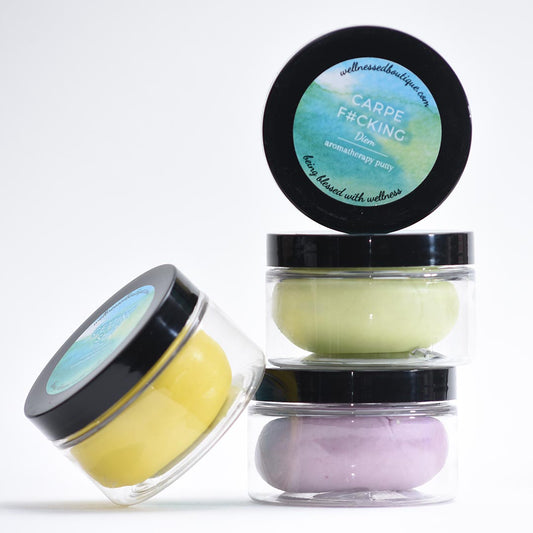 Four containers of Carpe Diem Aromatherapy Putty with black lids and colorful contents on a white background