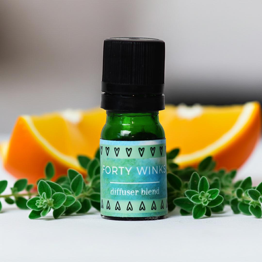 Bottle of 'Forty Winks' diffuser blend for sleep with orange slices and green leaves on a light background
