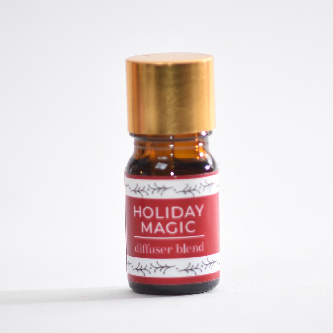 Small amber glass bottle labeled 'Holiday Magic diffuser blend' with a gold cap on a white background