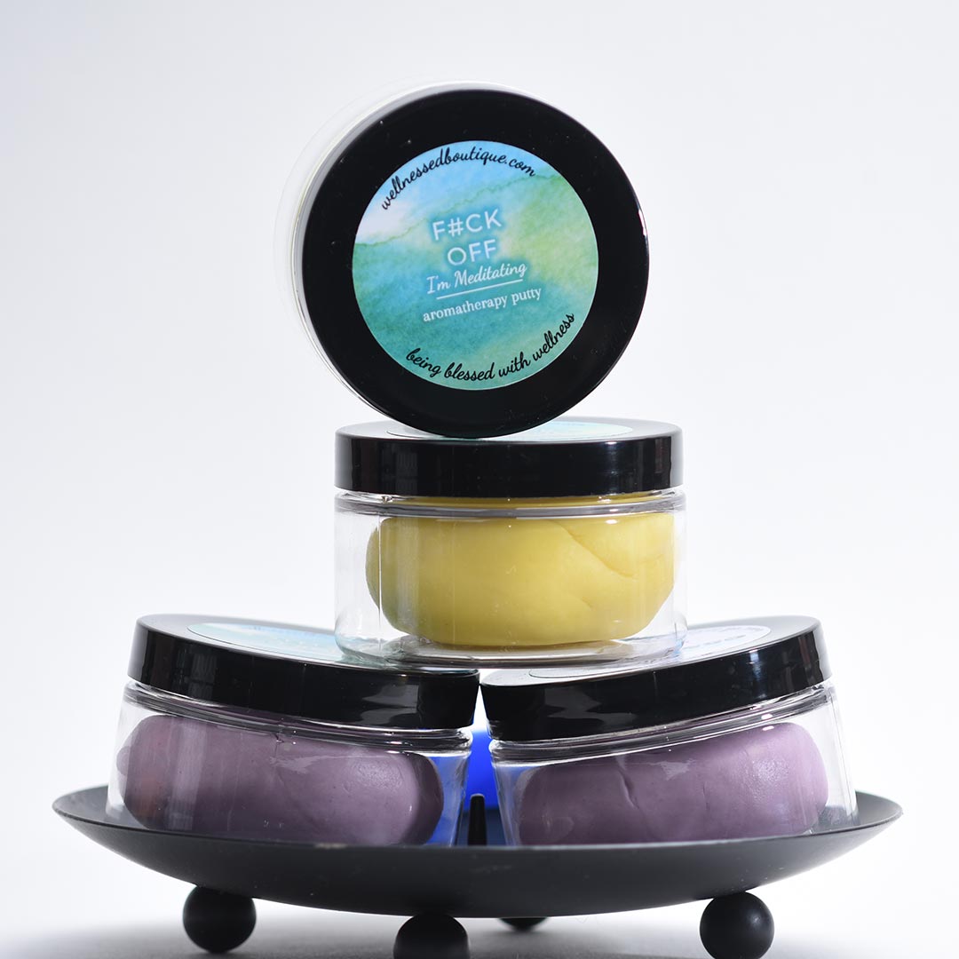 Four containers of I'm Meditating grounding aromatherapy sensory putty with lids on a white background