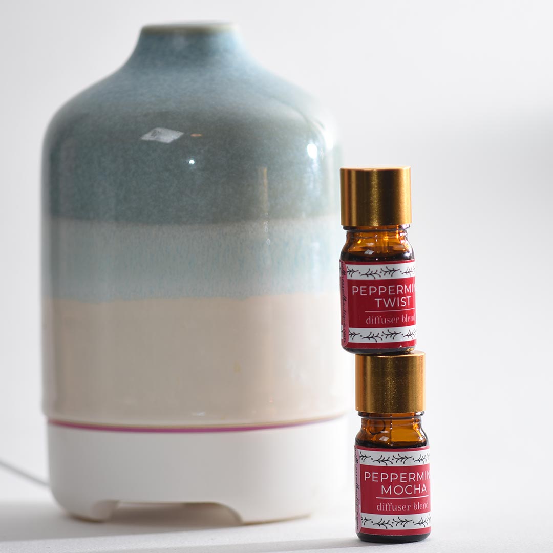 Two Peppermint Twist diffuser bottles in front of a ceramic vase on a white background